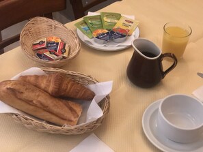 Een ontbijtje met croissants, een mok, een bord met porties en een glas sinaasappelsap op een tafel.
