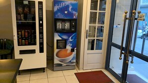 A coffee vending machine and a door with a glass panel, both in a public indoor space. - Liberty (Paris)