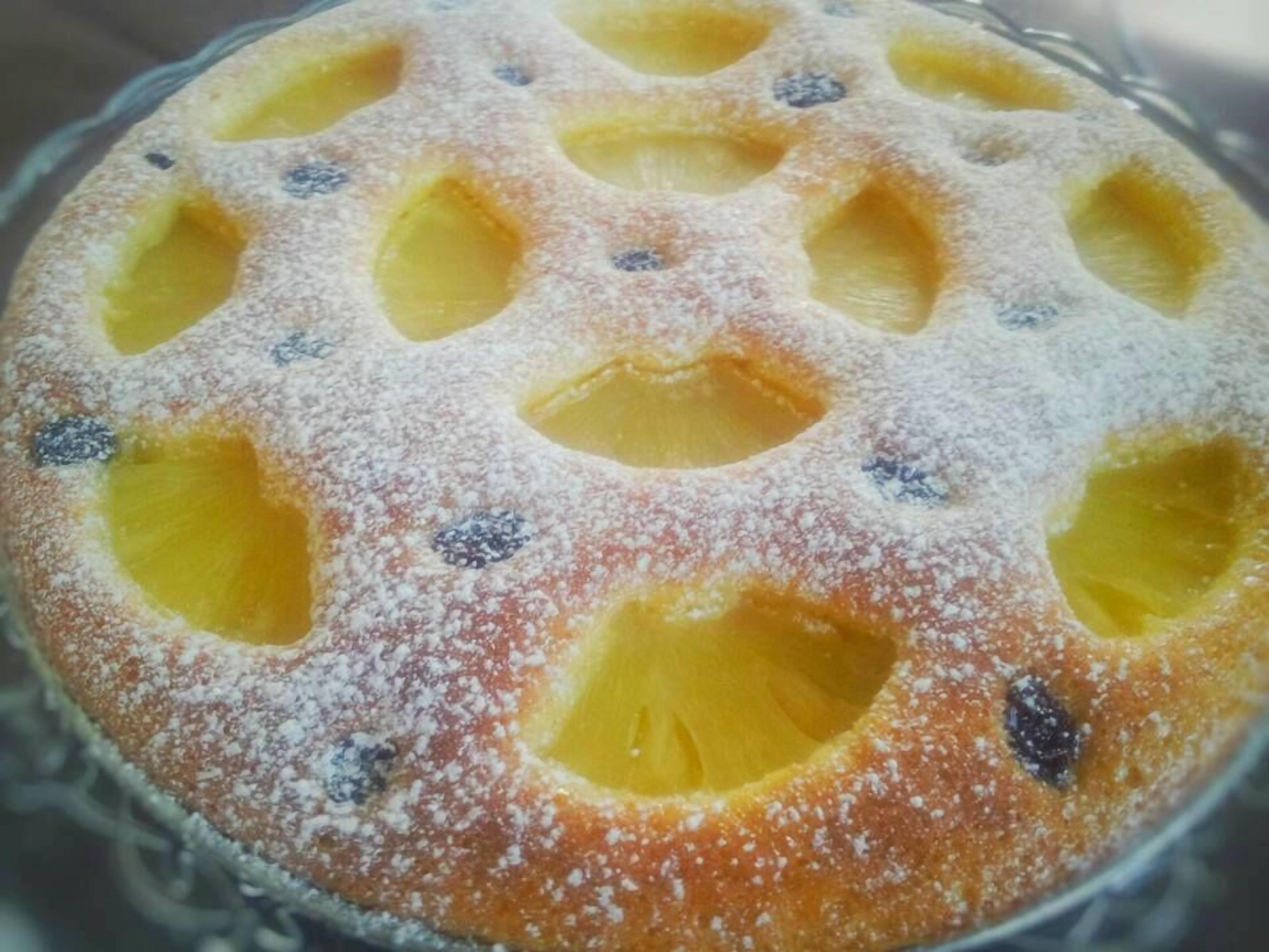 Ein runder Kuchen mit Ananasstücken und Blaubeeren, bestäubt mit Puderzucker.