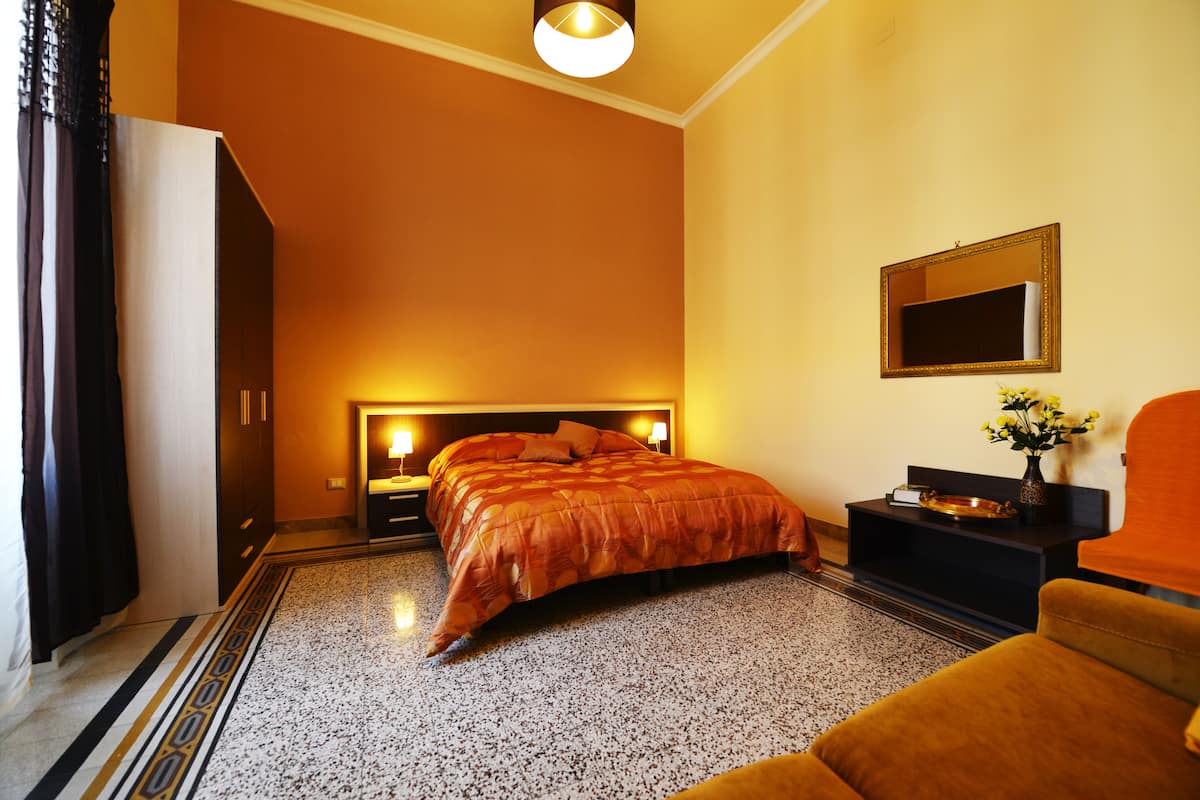A hotel room with a bed, a nightstand, a desk, a chair, and a mirror on the wall.
