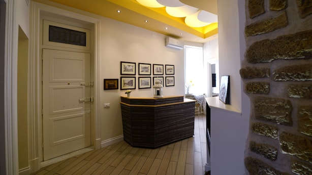 A reception area with a reception desk, framed pictures on the wall, a stone wall, and a wooden floor. - 174 Via Roma (Palermo)