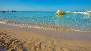 A beach with clear blue water, a sandy shore, and several small boats. - Constantinos The Great Beach Hotel (Paralimni)