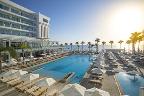 Ein Hotelpoolbereich mit mehreren Liegestühlen und Sonnenschirmen, freier Blick auf den Ozean sowie ein modernes Gebäude mit Balkonen.