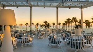 A rooftop lounge with white wicker furniture, a glass ceiling, and a view of the ocean at sunset. - Constantinos The Great Beach Hotel (Paralimni)