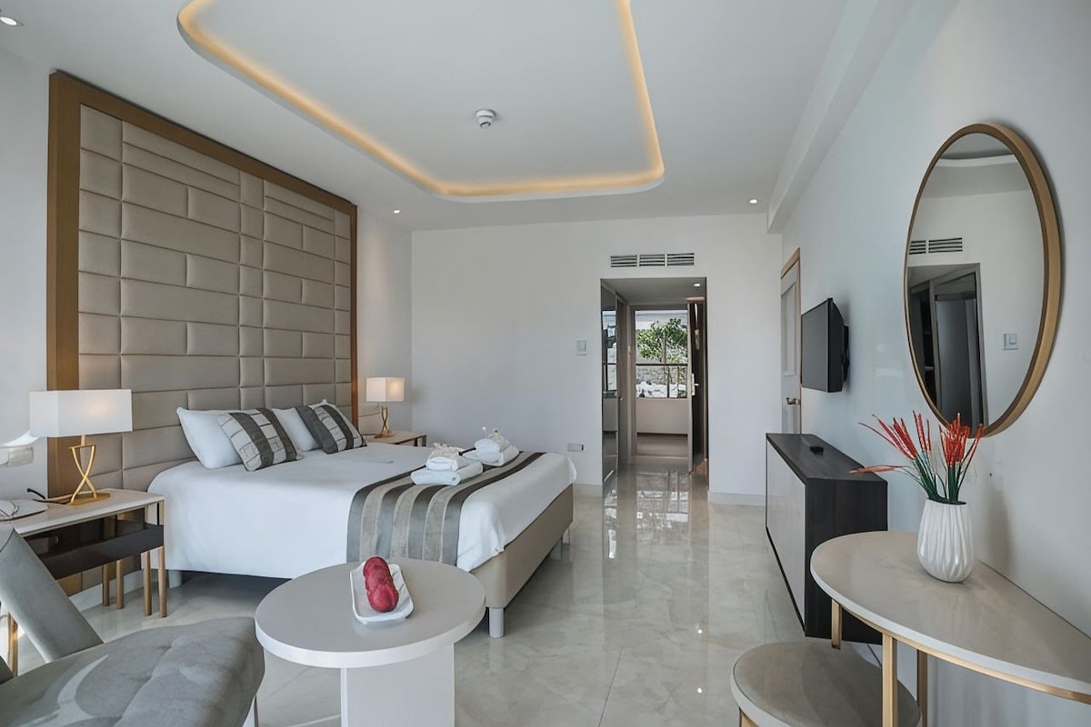Una habitación de hotel moderna con una cama grande, mesitas de noche, un escritorio y una mesa redonda.