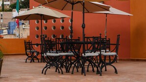 Un patio exterior con una mesa y sillas, rodeado de paredes naranjas con recortes circulares.