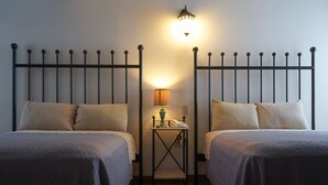Una habitación con dos camas, una mesita de noche con lámpara y una lámpara de pared.