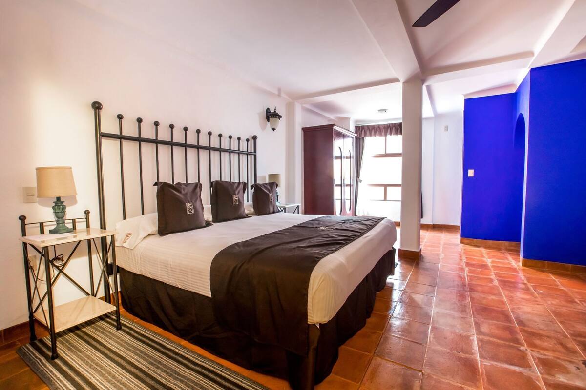 Habitació d'hotel amb un llit, una tauleta de nit, una làmpada i vista cap a l'exterior.