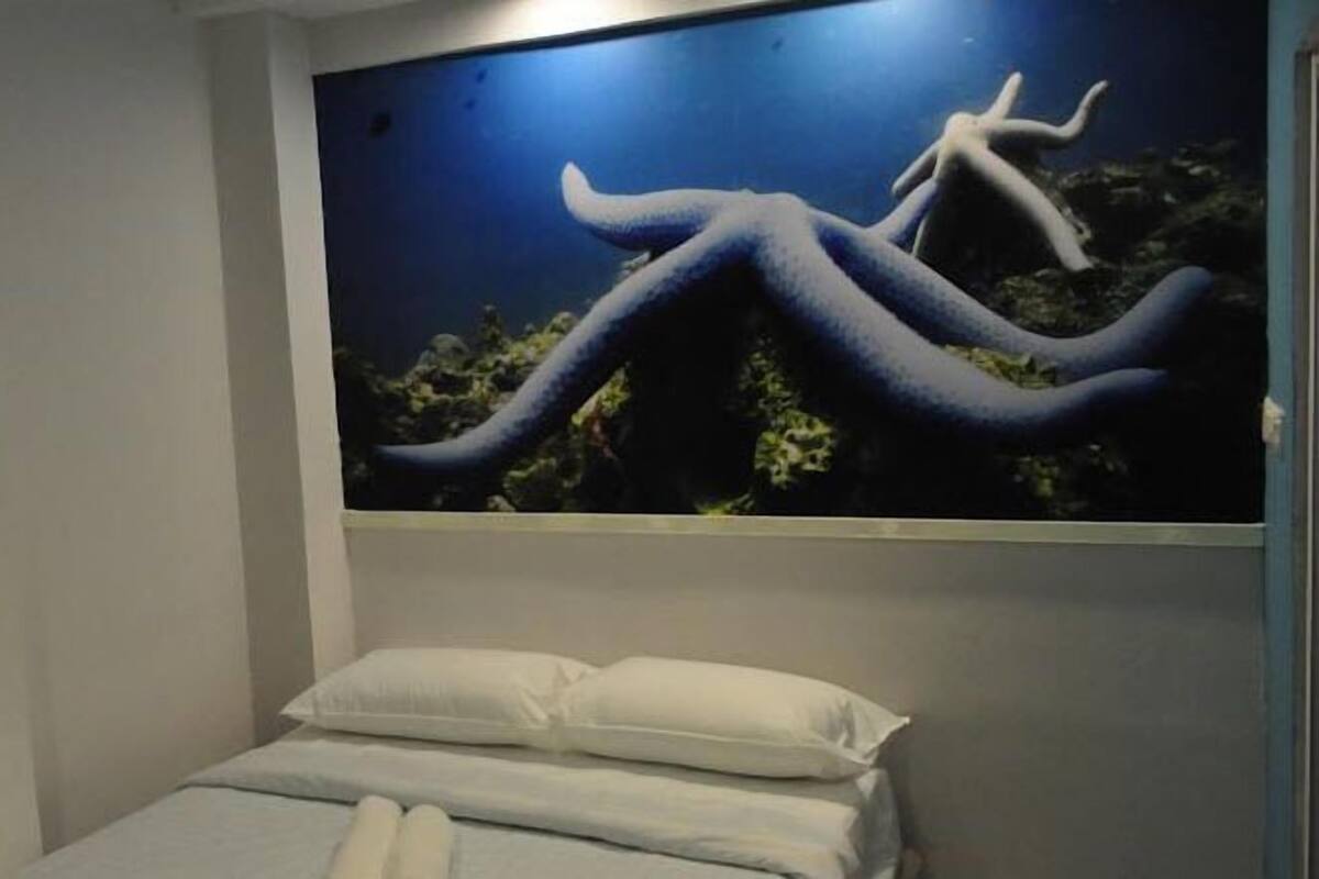 Een slaapkamer met een bed, witte kussens en een groot poster van een blauwe octopus aan de muur.
