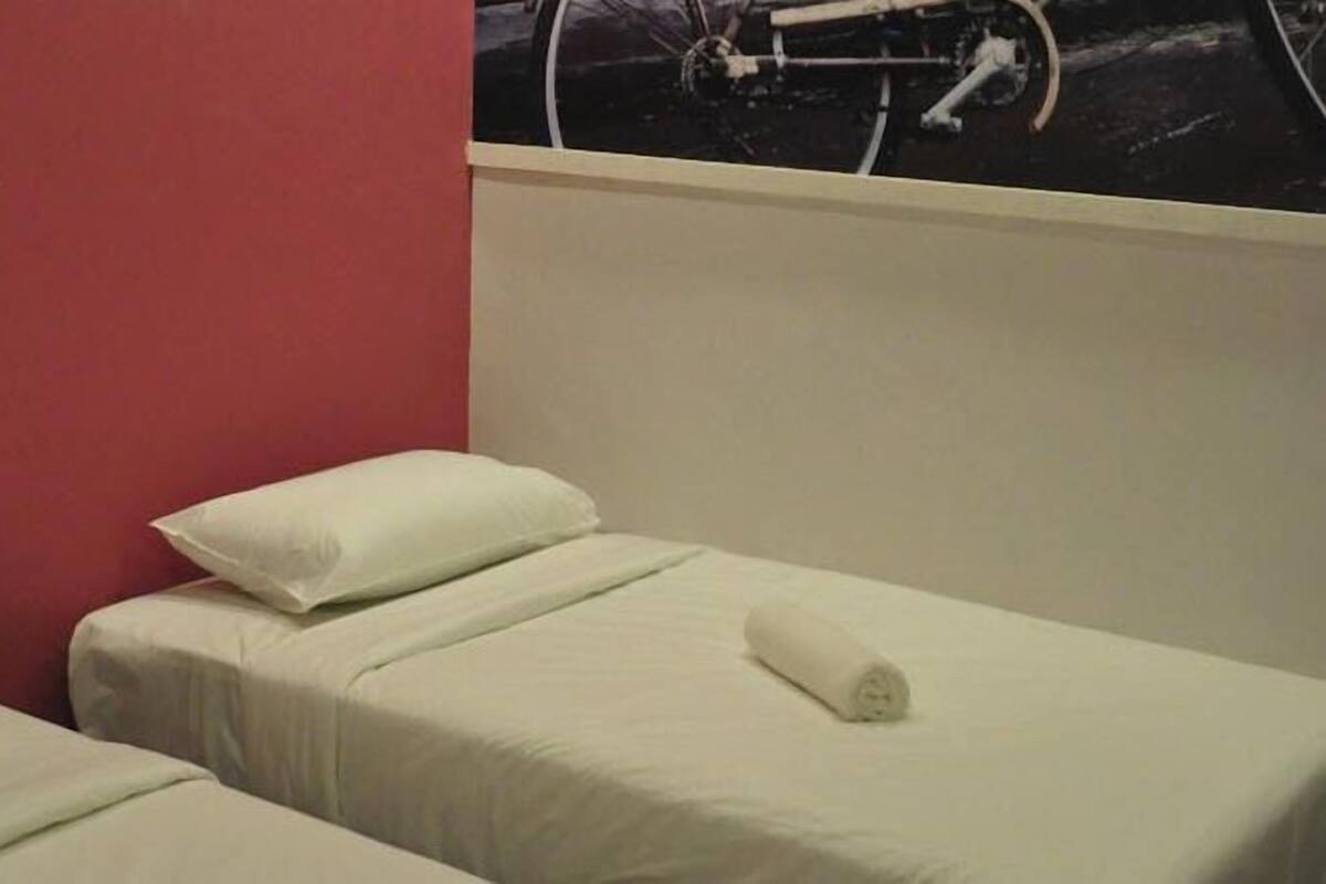 Een hotelkamer met twee enkele bedden, elk voorzien van een witte matras en kussen, en een rode wand.