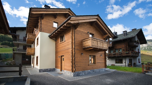 A wooden chalet with balconies, a stone foundation, and a clear sky. - Central Rin (Livigno)