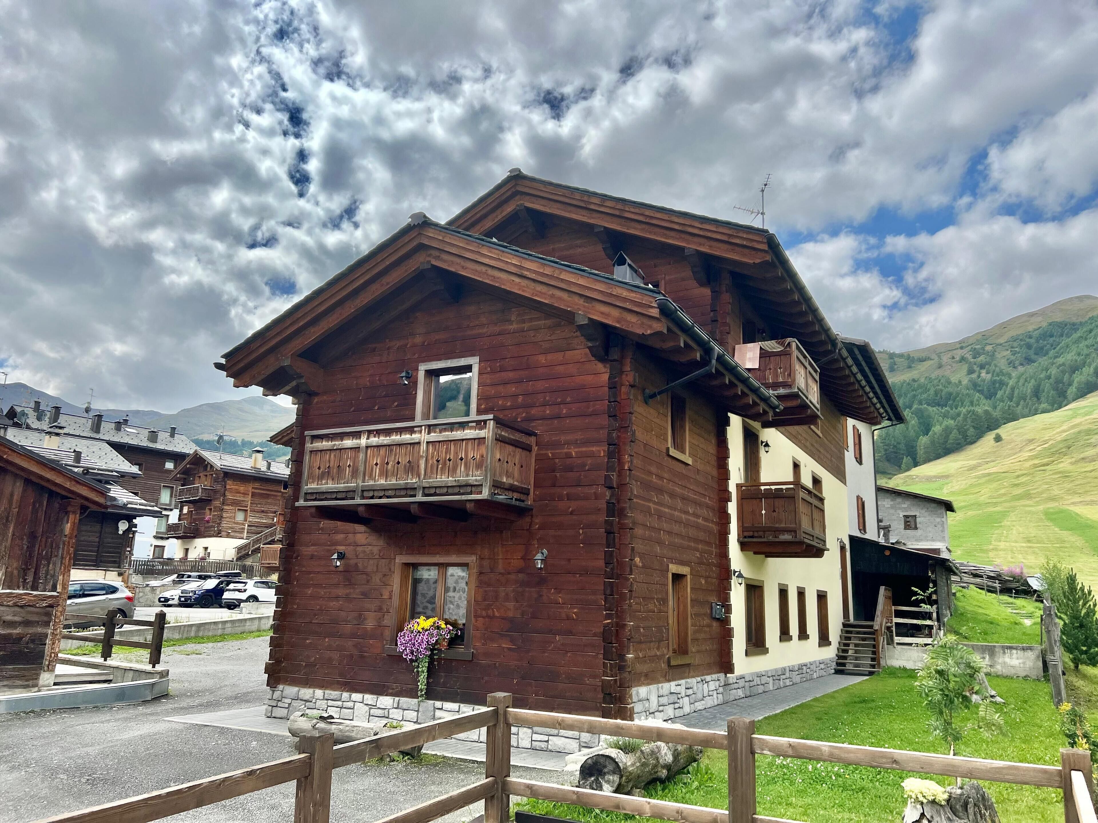 Un chalet en bois doté d’un balcon, de fondations en pierre et offrant une vue sur les collines environnantes.