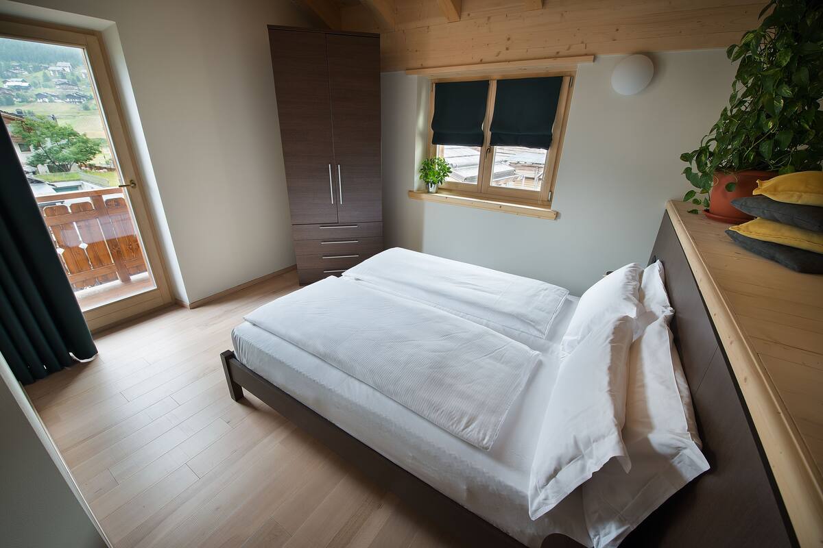 Un dormitorio con cama, armario, ventana con planta y vistas al exterior.