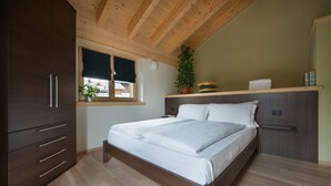 A bedroom with a wooden ceiling, a bed with white bedding, a dark wooden wardrobe, a window with a view, and a bedside plant. - Central Rin (Livigno)