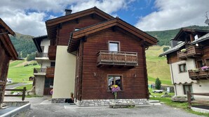A wooden chalet with a balcony, a stone foundation, and a view of the surrounding hills. - Central Rin (Livigno)