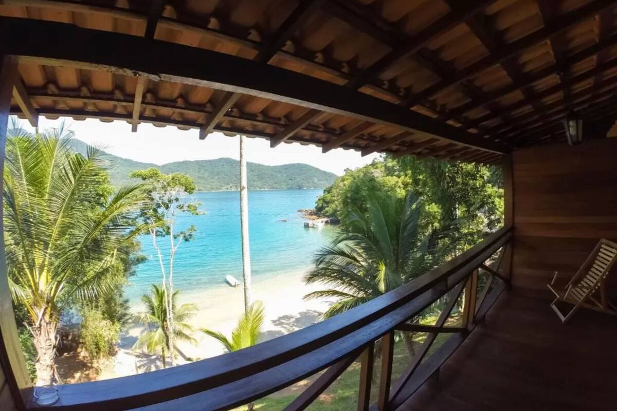 A wooden balcony with a view of a beach and palm trees.
