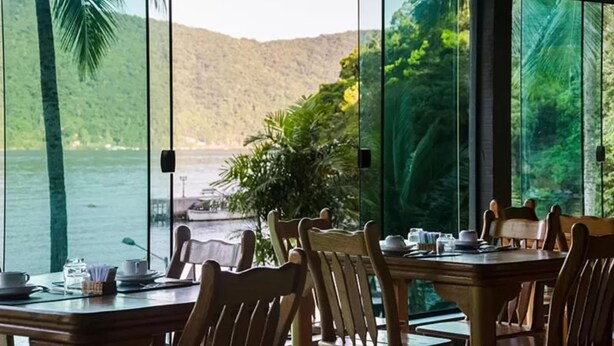 A dining area with a table set for two, overlooking a body of water and lush greenery. - Pousada Portal do Sol (Angra dos Reis)