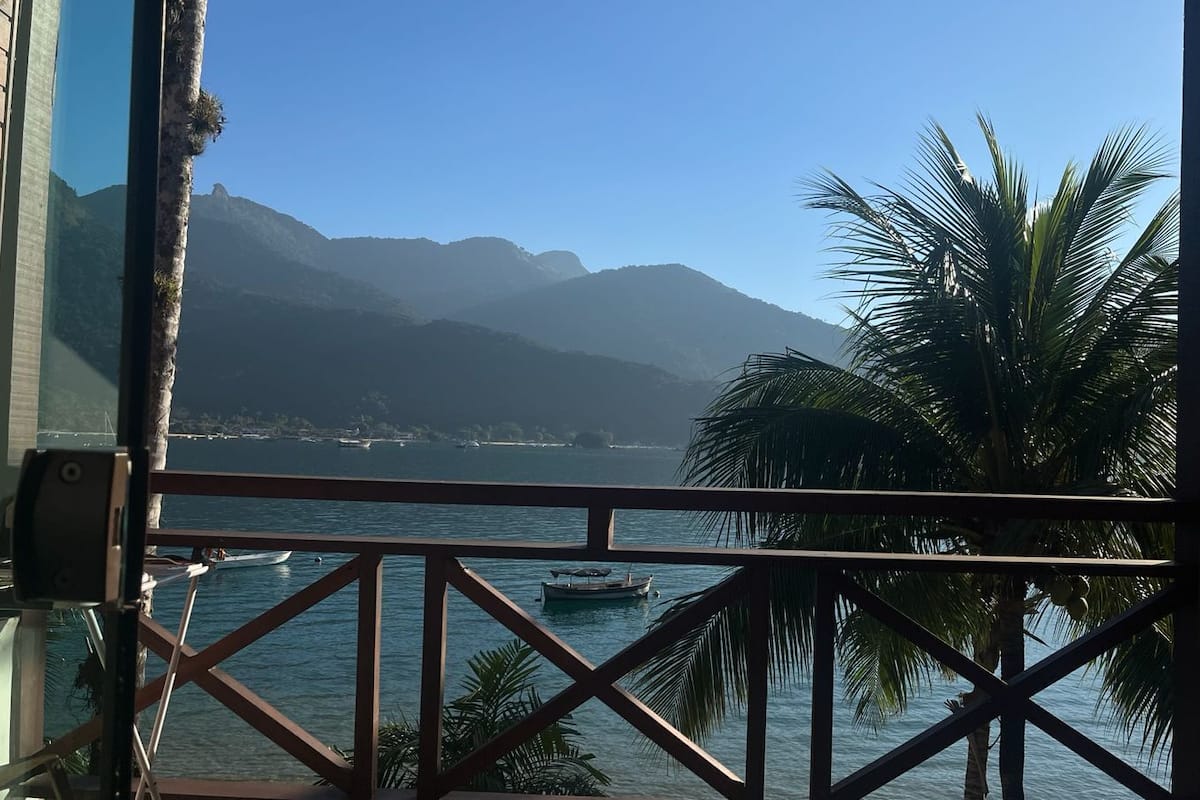 A balcony with a view of the sea, palm trees, and mountains.
