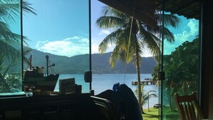 A room with a large window overlooking a lake, a desk with a computer, and a chair. - Pousada Portal do Sol (Angra dos Reis)