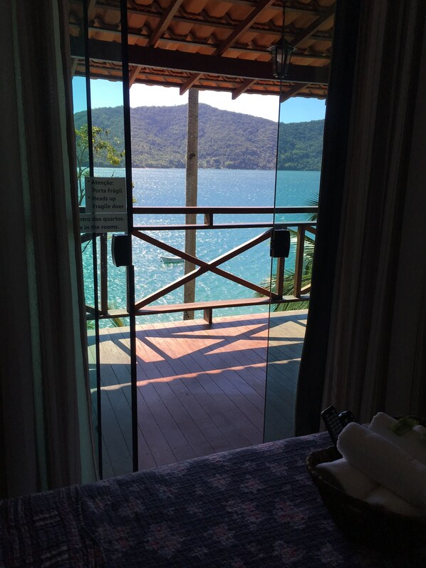 A view from a room with a wooden deck overlooking a lake, a sign warning of a fragile door, and a remote control on the table.