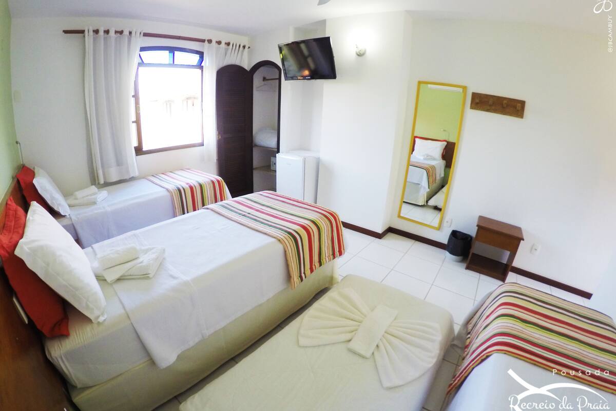 Quarto de hotel com duas camas, televisão, espelho e janela com cortinas.