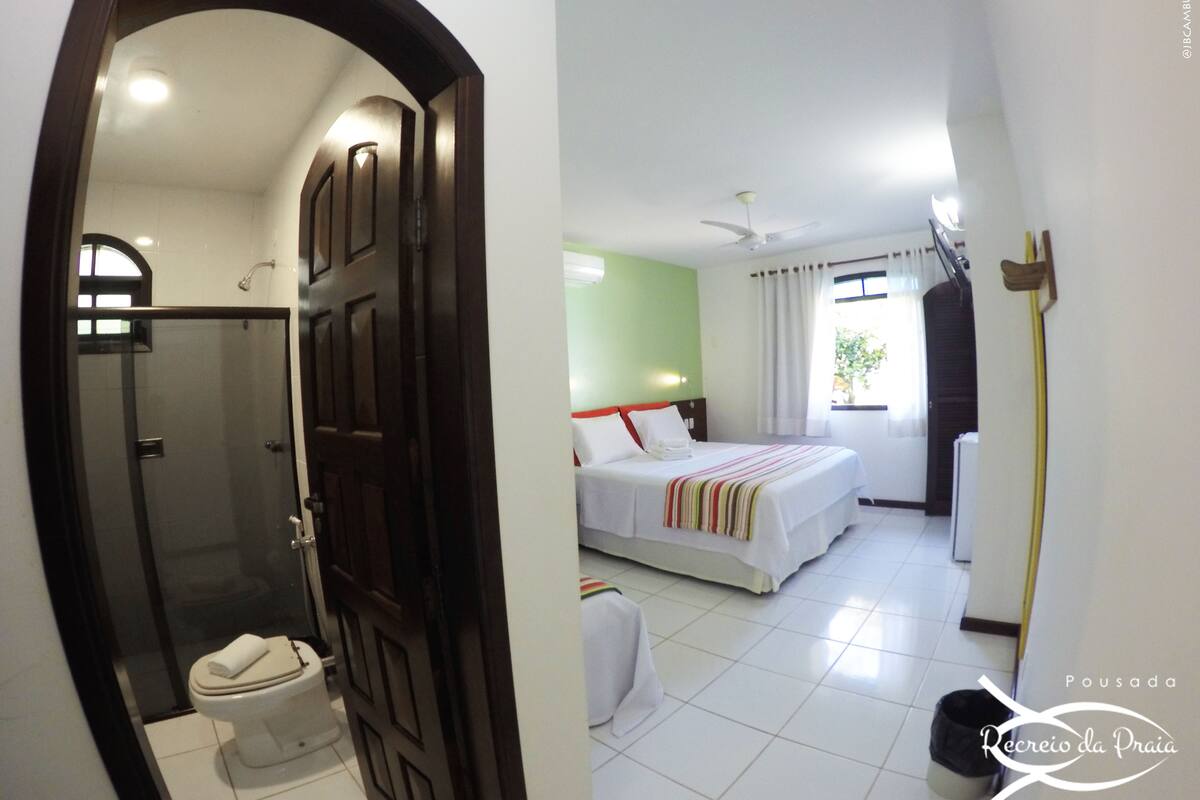 Quarto de hotel com chuveiro, vaso sanitário, cama e janela com cortinas.