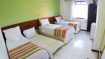 A hotel room with three single beds, a ceiling fan, an air conditioner, and a window with curtains.