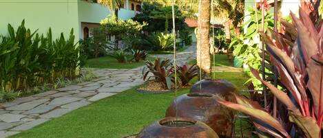 Un patio con un sendero de piedra, grandes macetas metálicas y exuberante vegetación tropical.