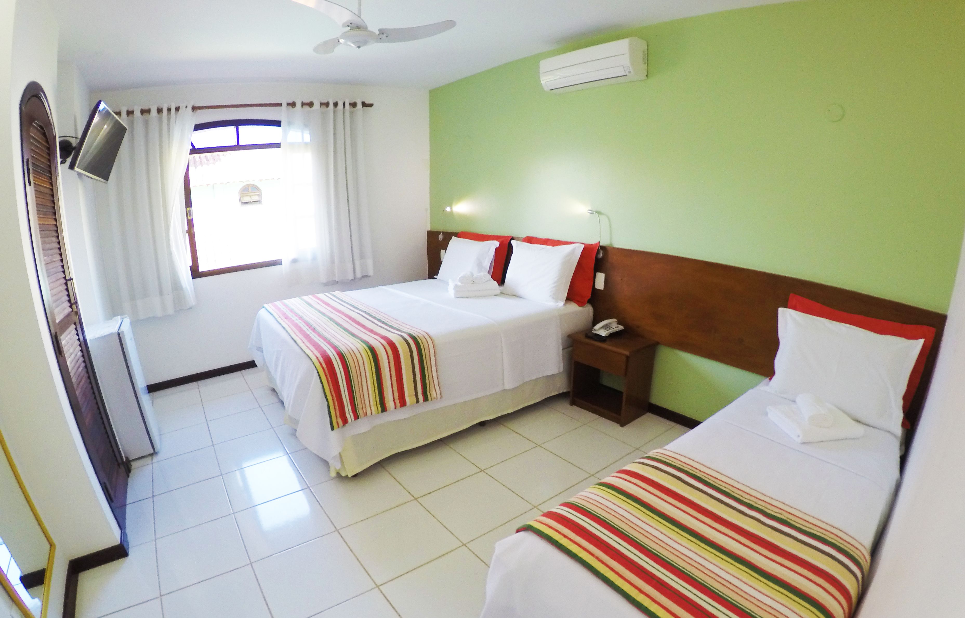 A hotel room with two beds, a TV, a ceiling fan, and a window with curtains.