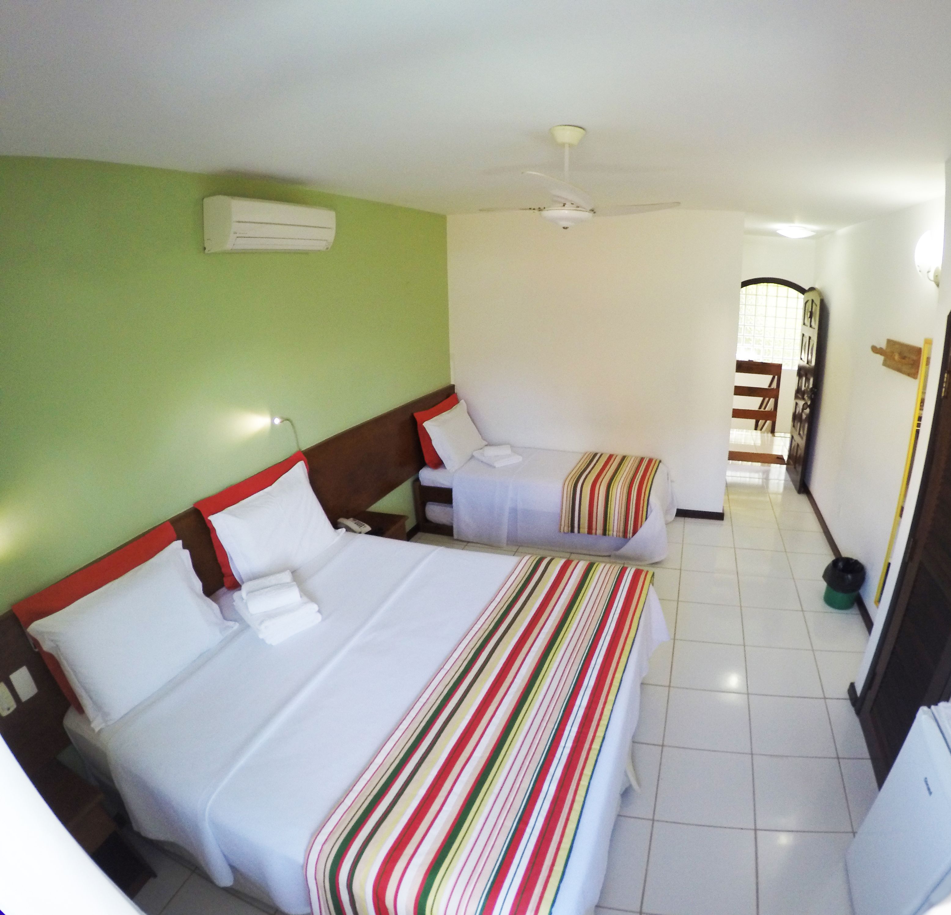 Habitación de hotel con dos camas, ventilador de techo y vista a un pasillo.