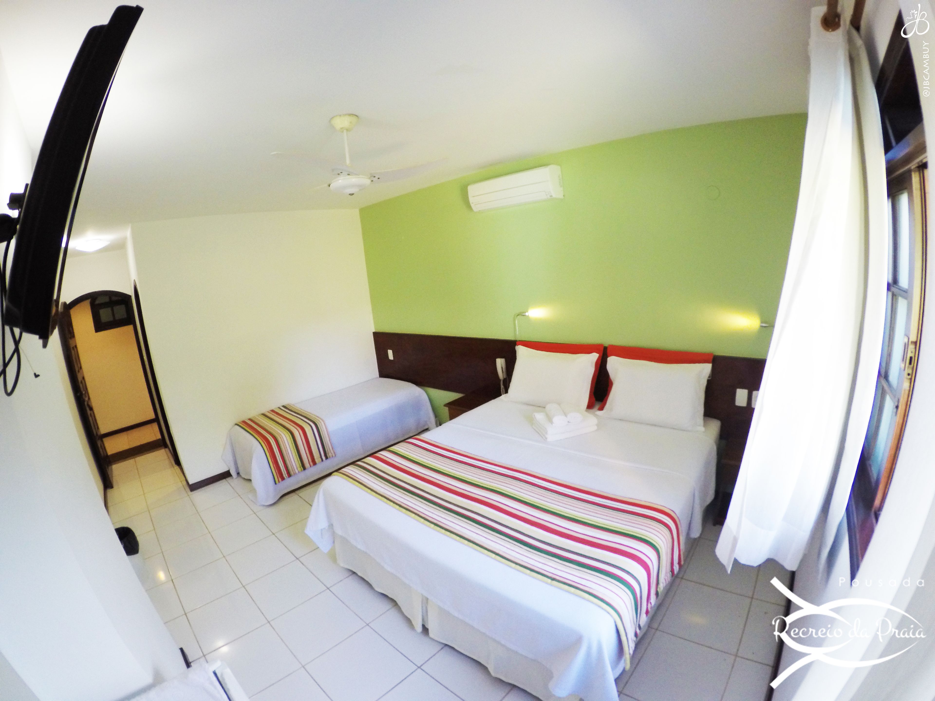 A hotel room with two beds, a ceiling fan, a TV mounted on the wall, and a window with curtains.