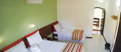 Habitación de hotel con dos camas, ventilador de techo y vista a un pasillo.