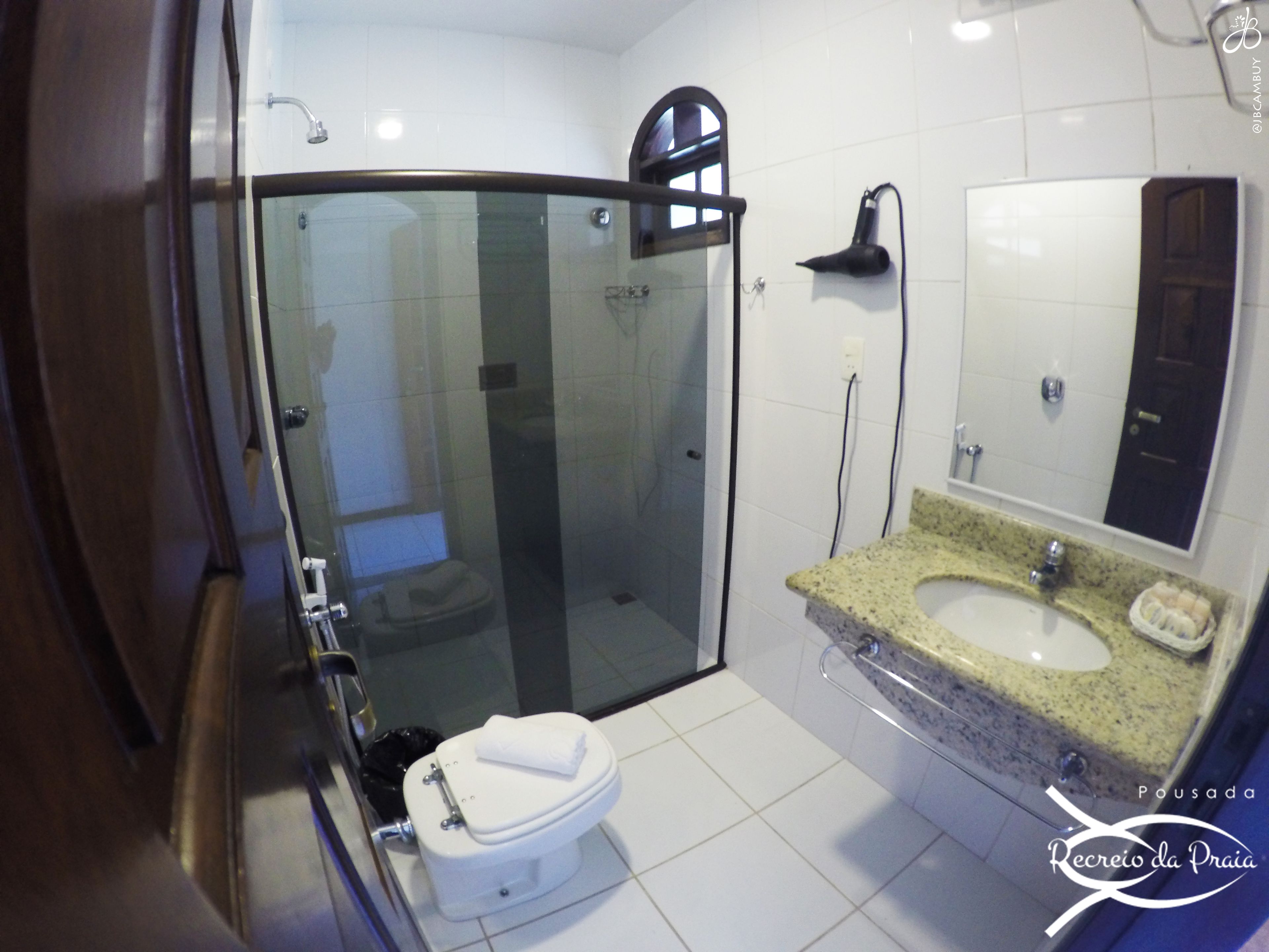Un baño moderno con ducha de vidrio, inodoro blanco y lavamanos sobre encimera de granito.