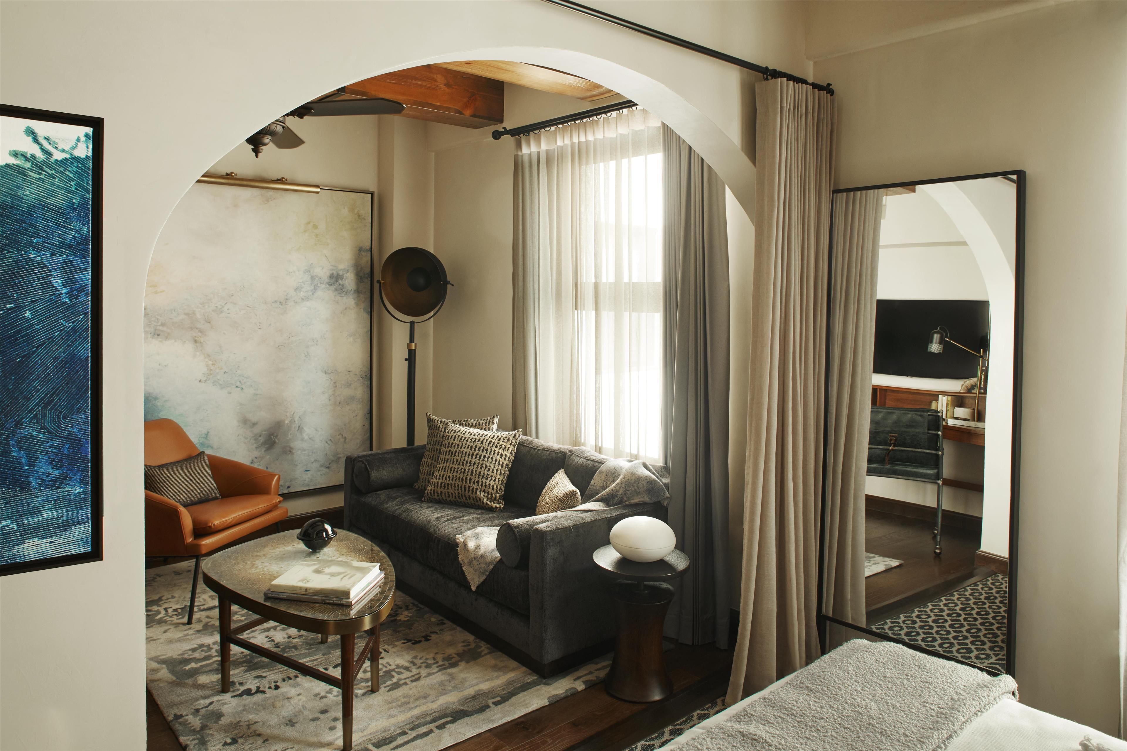 Un salon moderne comprenant un canapé, un fauteuil et une table basse, agrémenté d’un grand miroir et offrant une vue sur un balcon.