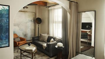 A modern living room with a sofa, armchair, and coffee table, featuring a large mirror and a view of a balcony.