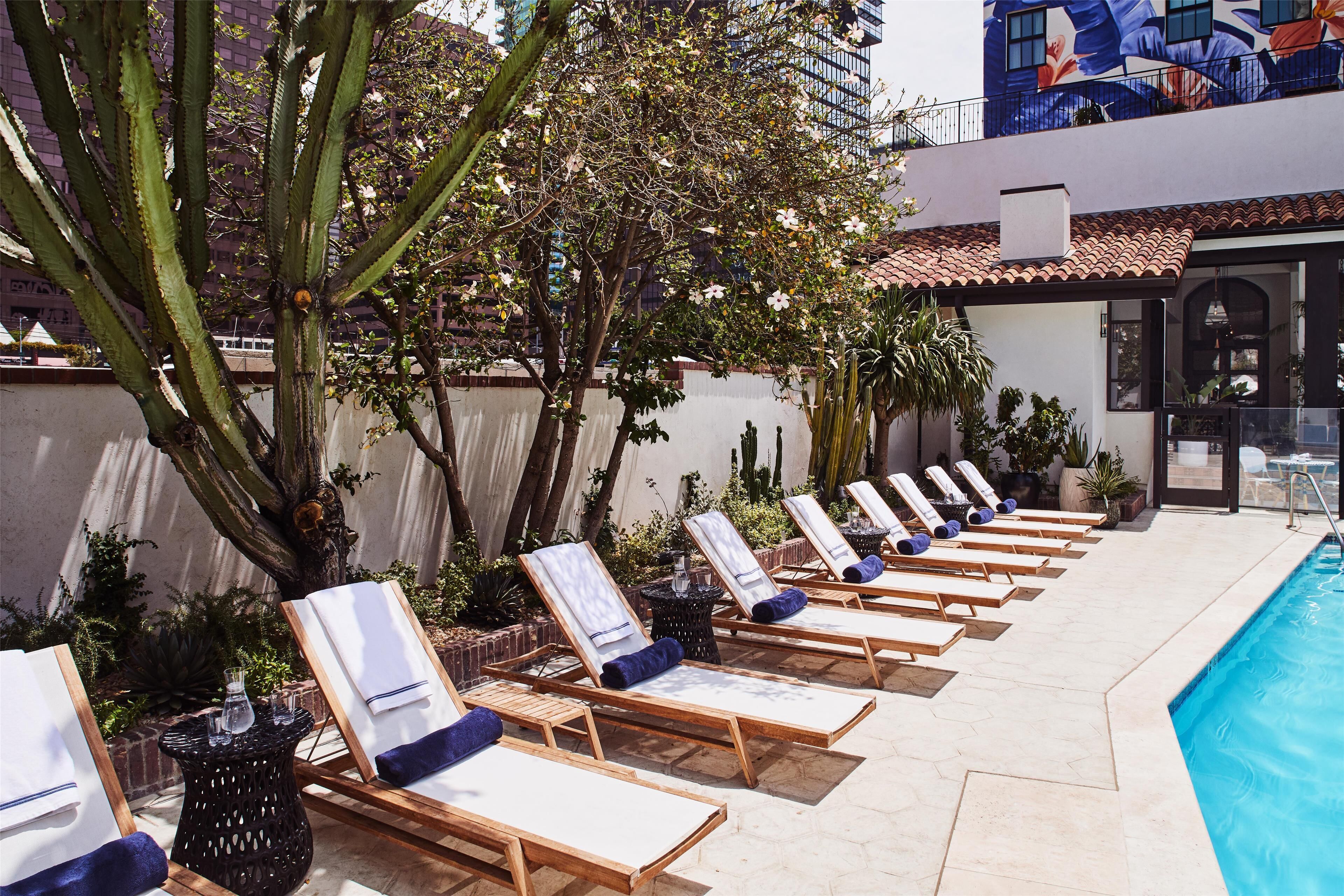A poolside area with sun loungers, a pool, and a building with a mural in the background.