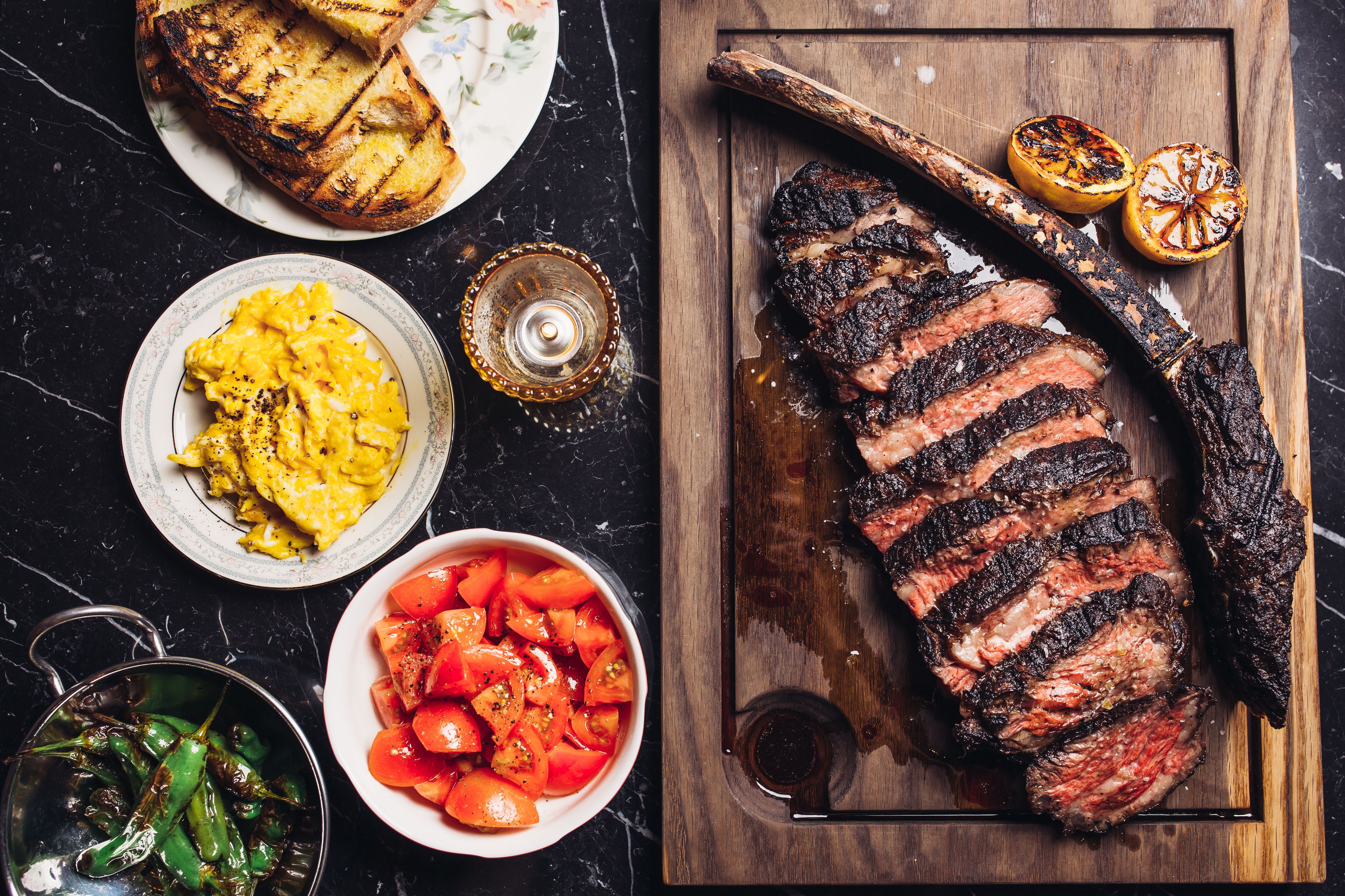 Un steak marqué par les traces du grill, un bol de tomates et une assiette d’œufs brouillés.