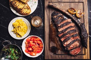Un filete con marcas de parrilla, un tazón de tomates y un plato de huevos revueltos.
