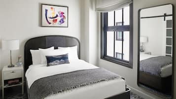 Une chambre d’hôtel bien rangée, avec un lit, une table de chevet, une lampe, un tableau encadré, une fenêtre donnant sur un beau paysage et un miroir.