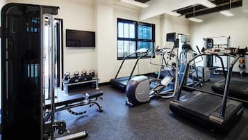 Une salle de sport équipée de tapis de course, d’une machine de musculation et de kettlebells.
