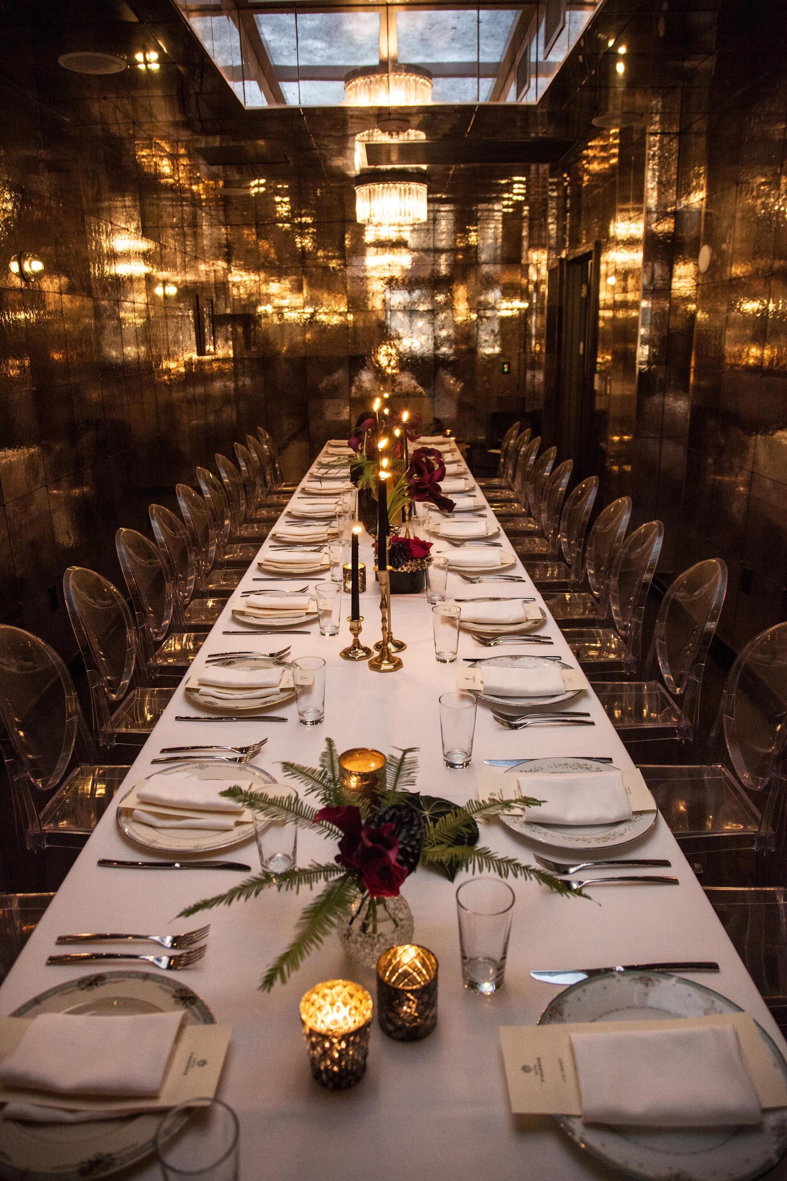 Een lange eettafel gedekt voor een formeel diner, met helder glaswerk, kaarsen en een bloemstuk.