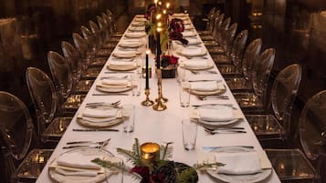 Une longue table à manger, dressée pour un repas formel, avec de la belle verrerie, des bougies et un arrangement floral en guise de centre de table.
