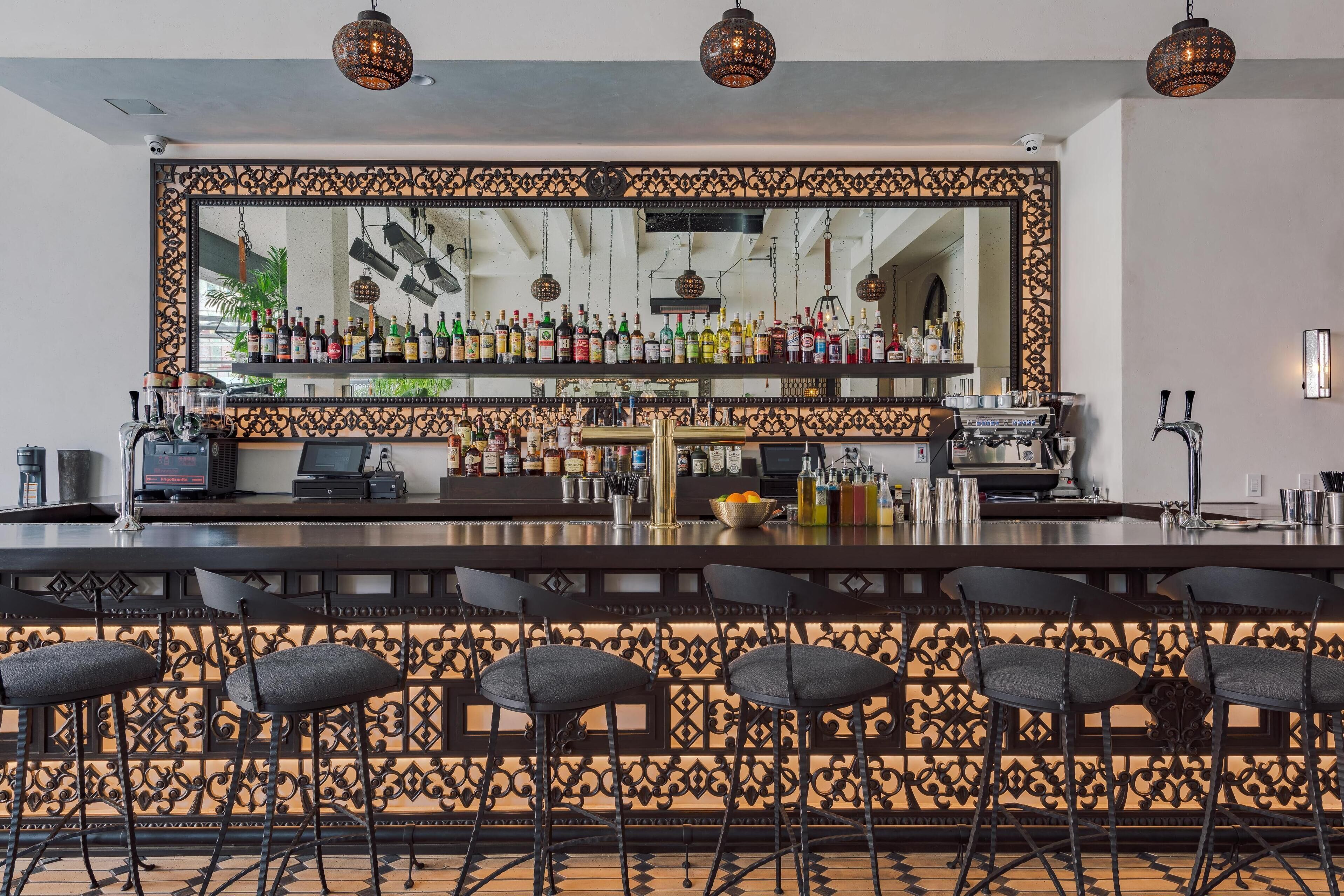 Eine Bar mit Spiegelwand, Barhocker und einer Auswahl an Flaschen und Gläsern.