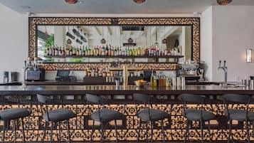 A bar area with a mirrored wall, bar stools, and a variety of bottles and glasses.