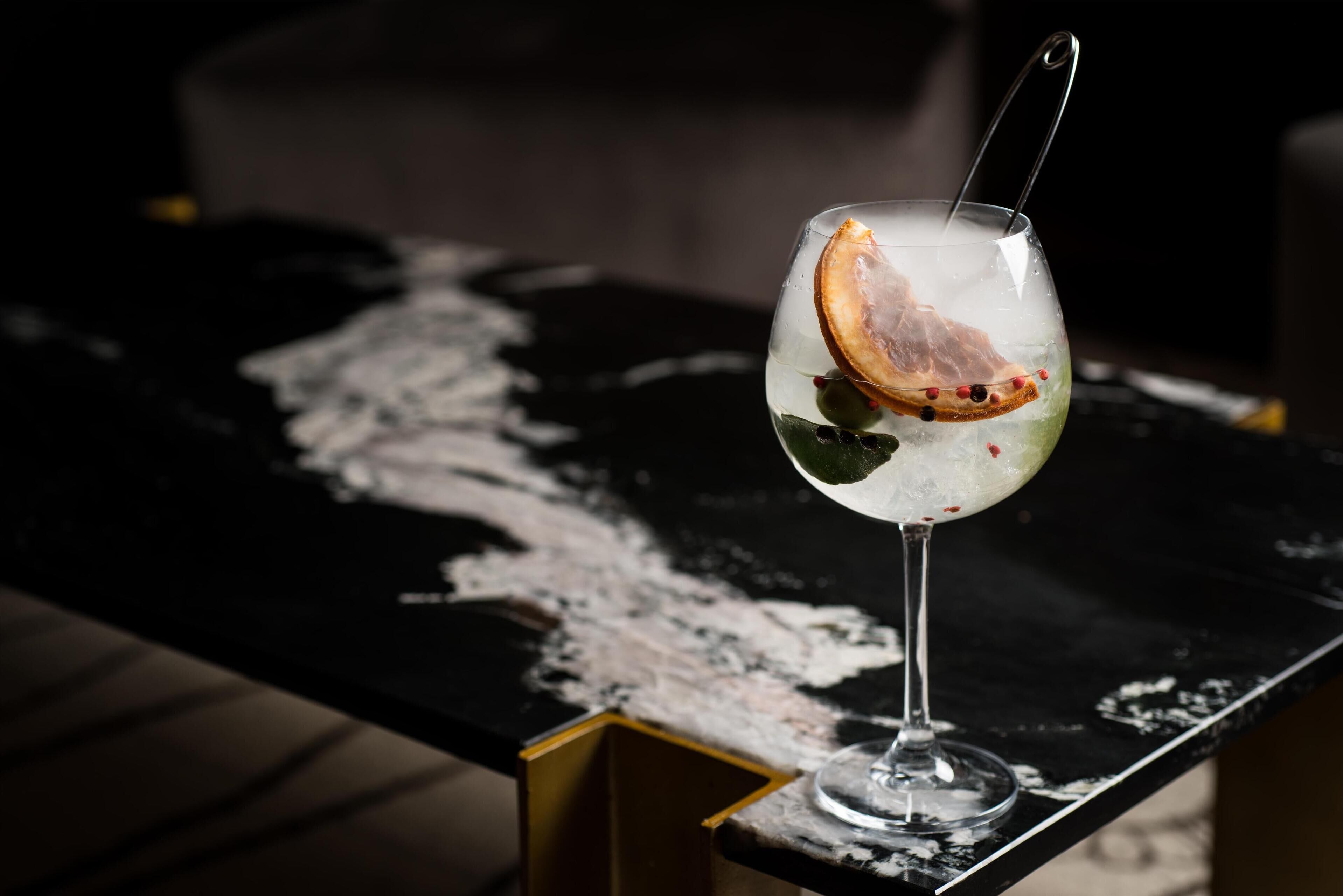 Un verre contenant une tranche d’orange et des olives, posé sur une surface noire.