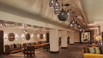 A spacious lobby with a long bench seating area, multiple hanging light fixtures, and a staircase leading to an upper level.