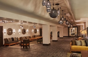 A spacious lobby with a long bench seating area, multiple hanging light fixtures, and a staircase leading to an upper level.