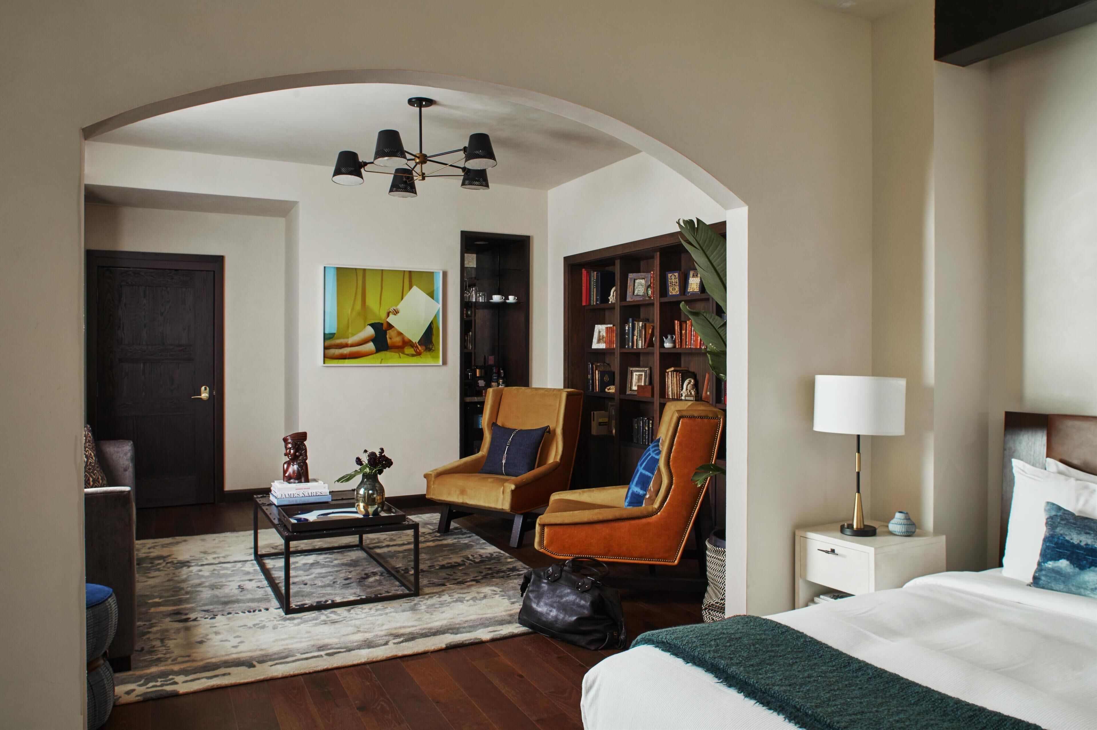 Une chambre d’hôtel moderne avec un grand lit, un canapé, une table basse, une bibliothèque et un tableau au mur.