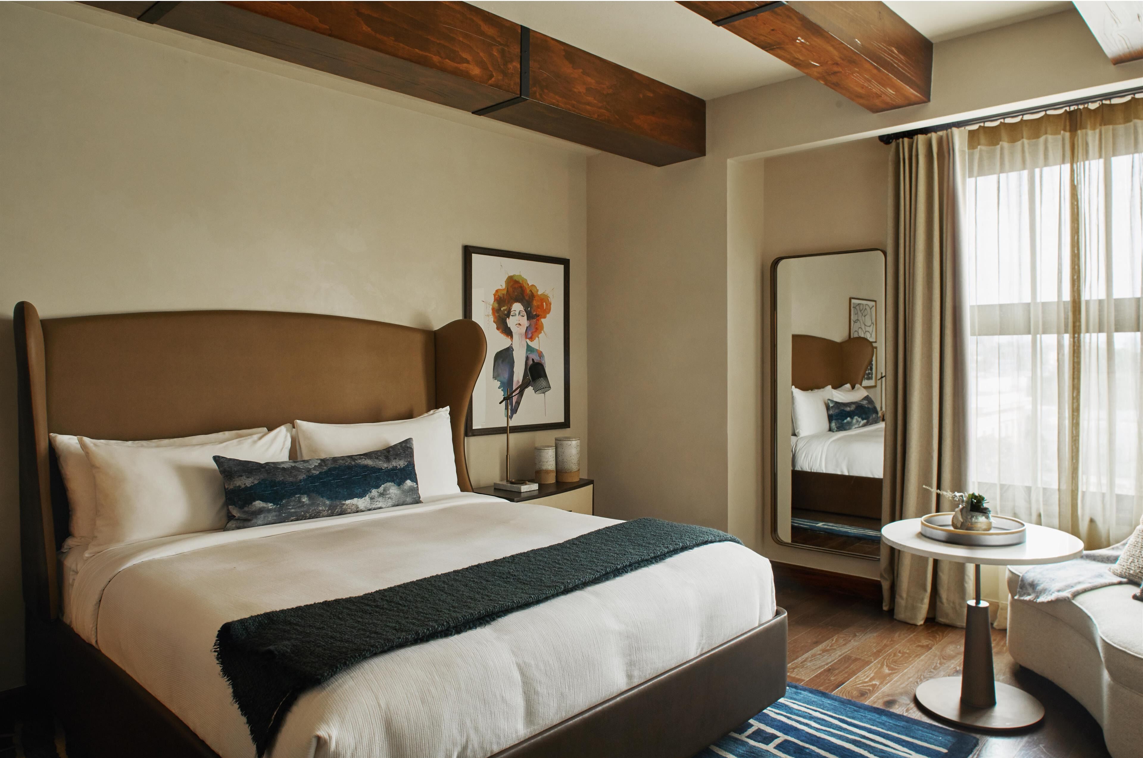 A hotel room with a large bed, a bedside table, a chair, a round table, and a mirror.