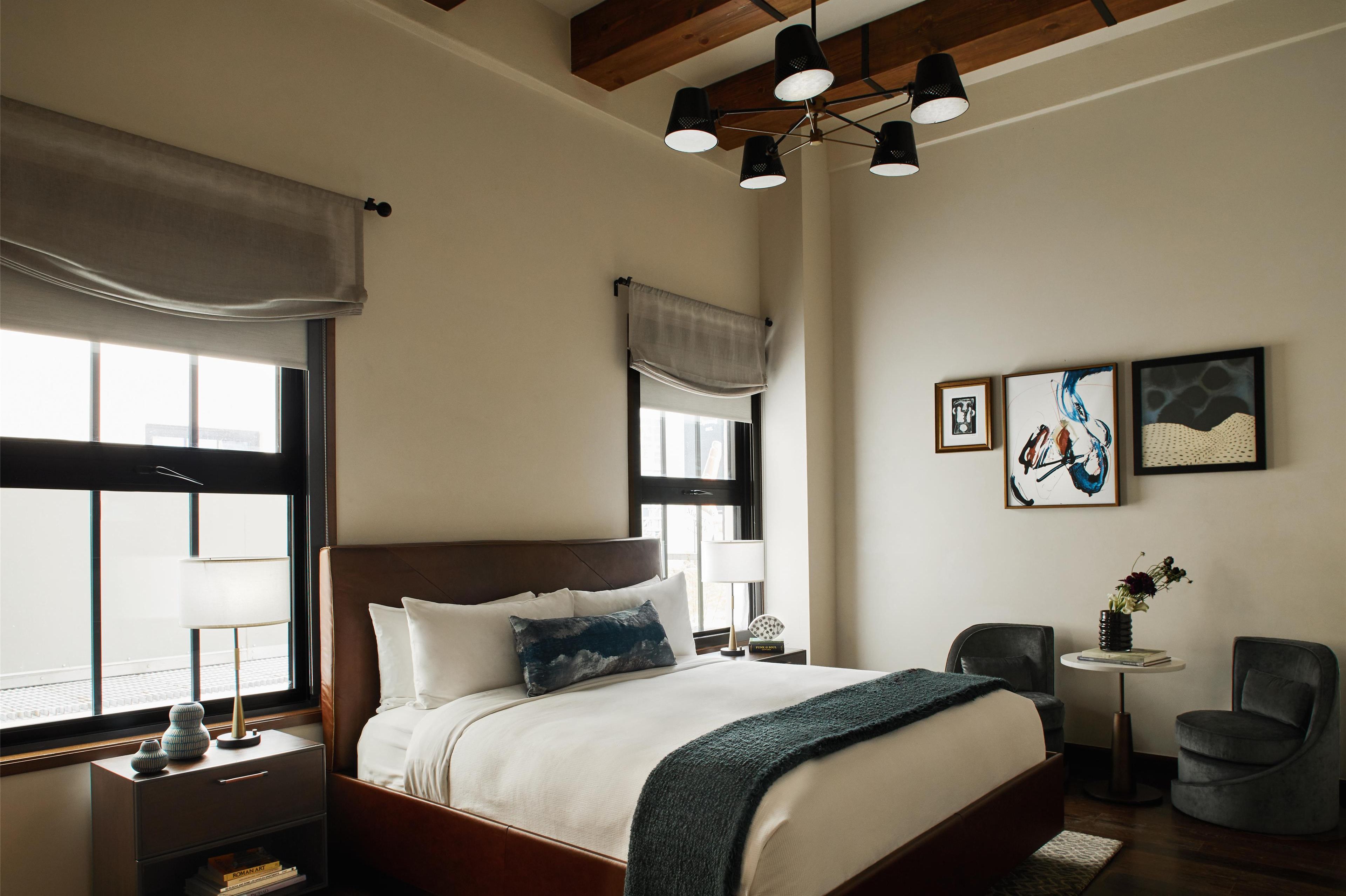 A neatly arranged bedroom with a large bed, bedside tables, a small table with a vase, and artwork on the wall.